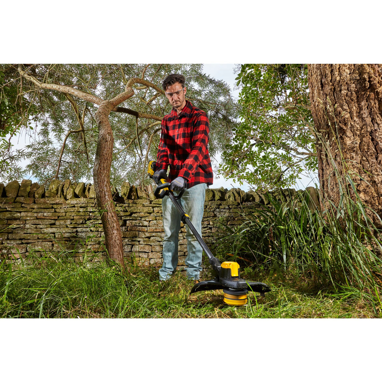 Homme utilisant une débroussailleuse DeWalt, outil de jardin jaune et noir, dans un jardin.