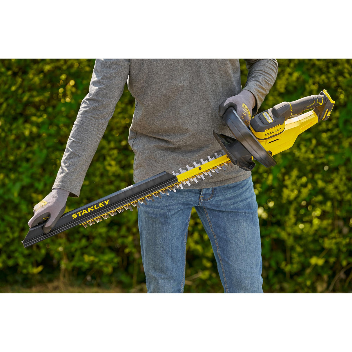 Taille-haie électrique Stanley jaune et noir, outil de jardinage en main, utilisé en extérieur.