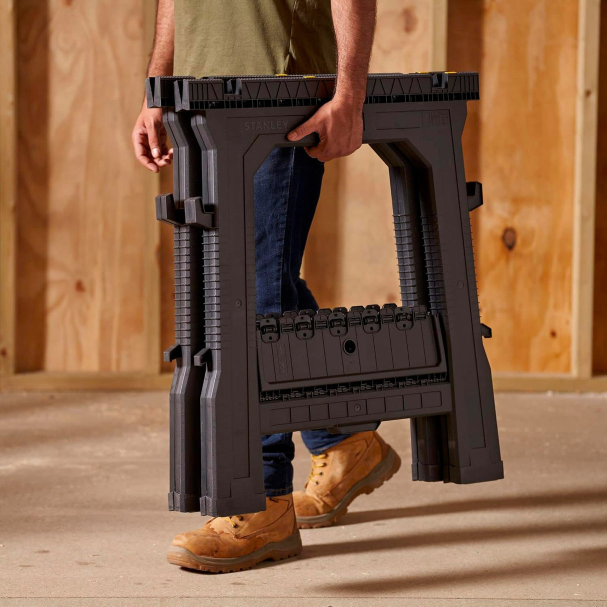 Tréteau pliant noir Stanley, outil de support portable, porté par un homme sur chantier