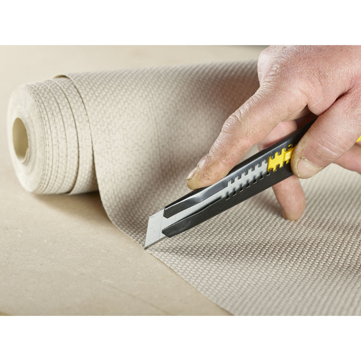 Cutter Stanley, couteau universel noir et jaune, utilisé pour découper un tapis beige.