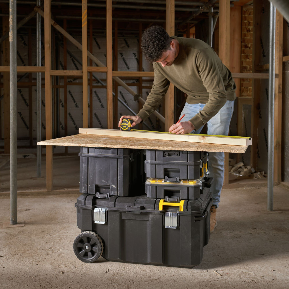 Coffre à outils noir Stanley, homme travaillant sur chantier, valise à roulettes