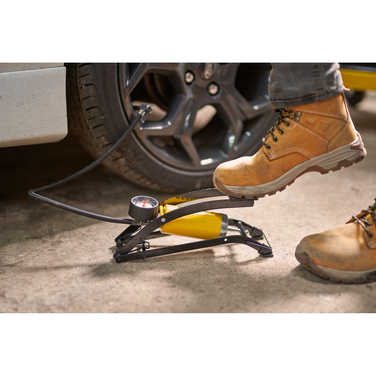 Pompe à pied Stanley jaune pour gonfler pneus de voiture, avec manomètre, en usage.