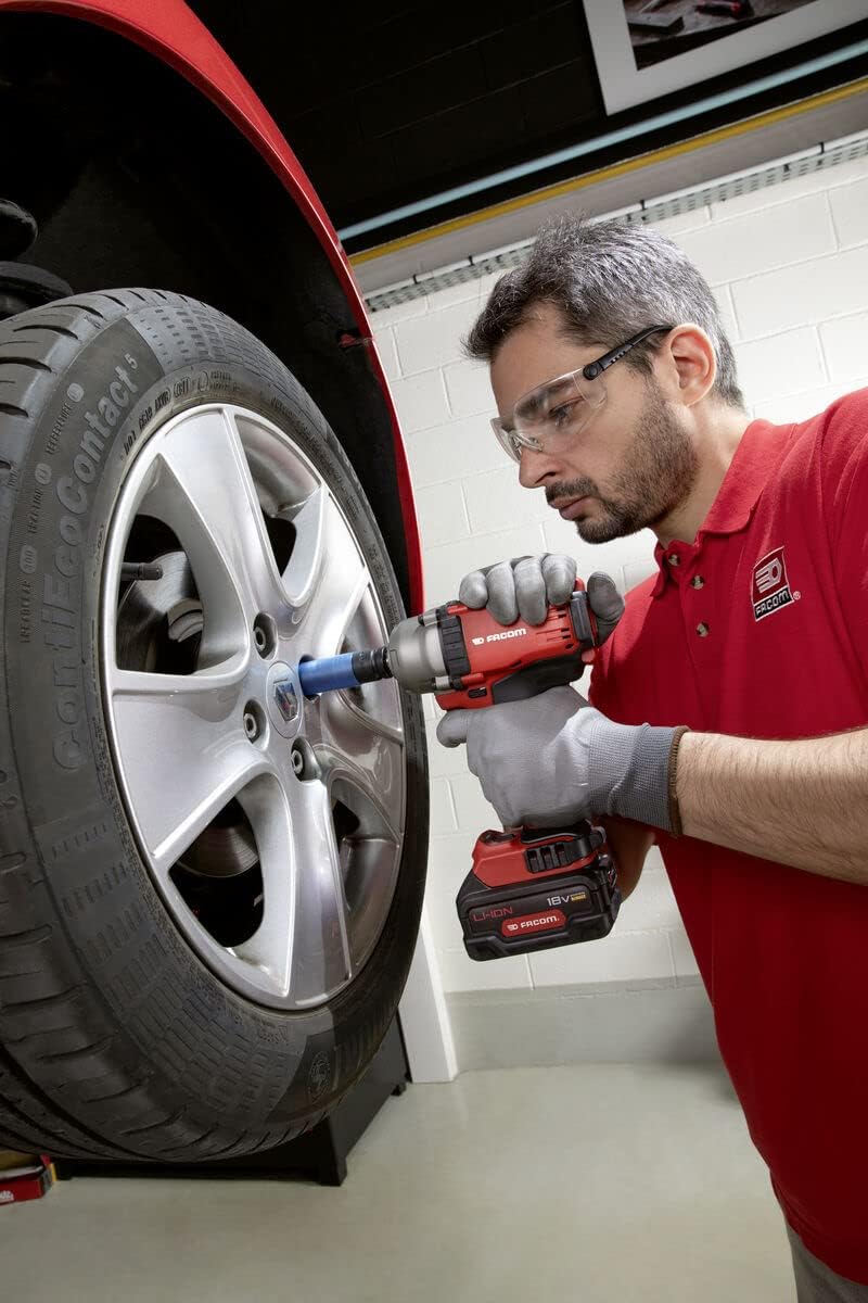 Homme utilisant une clé à chocs rouge Facom pour desserrer une roue de voiture argentée