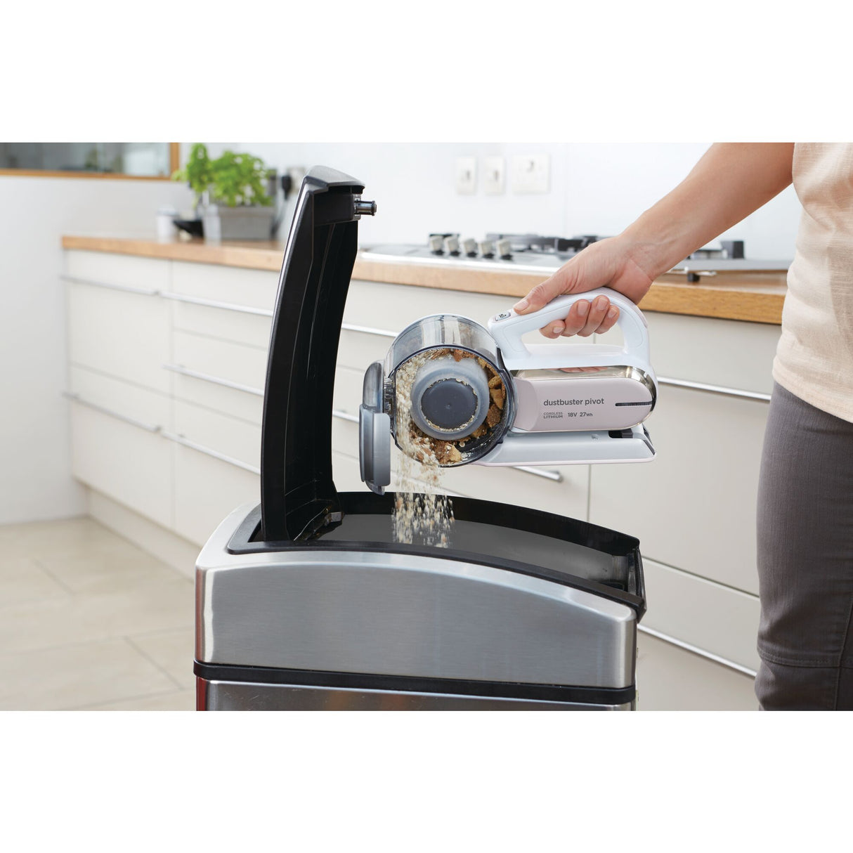 Aspirateur à main Black+Decker blanc utilisé pour vider la poussière dans une cuisine moderne.