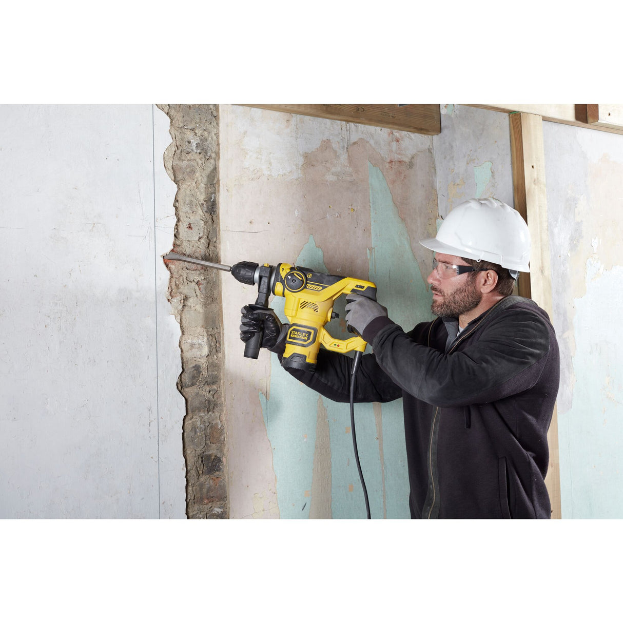 Perforateur Stanley jaune utilisé par un ouvrier sur un mur, outil électroportatif.