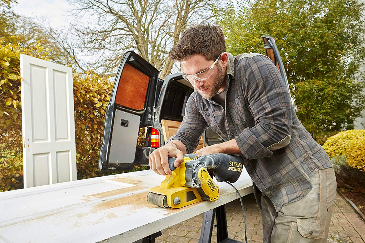 Homme utilisant une ponceuse électrique Stanley FATMAX jaune pour poncer une porte en bois.