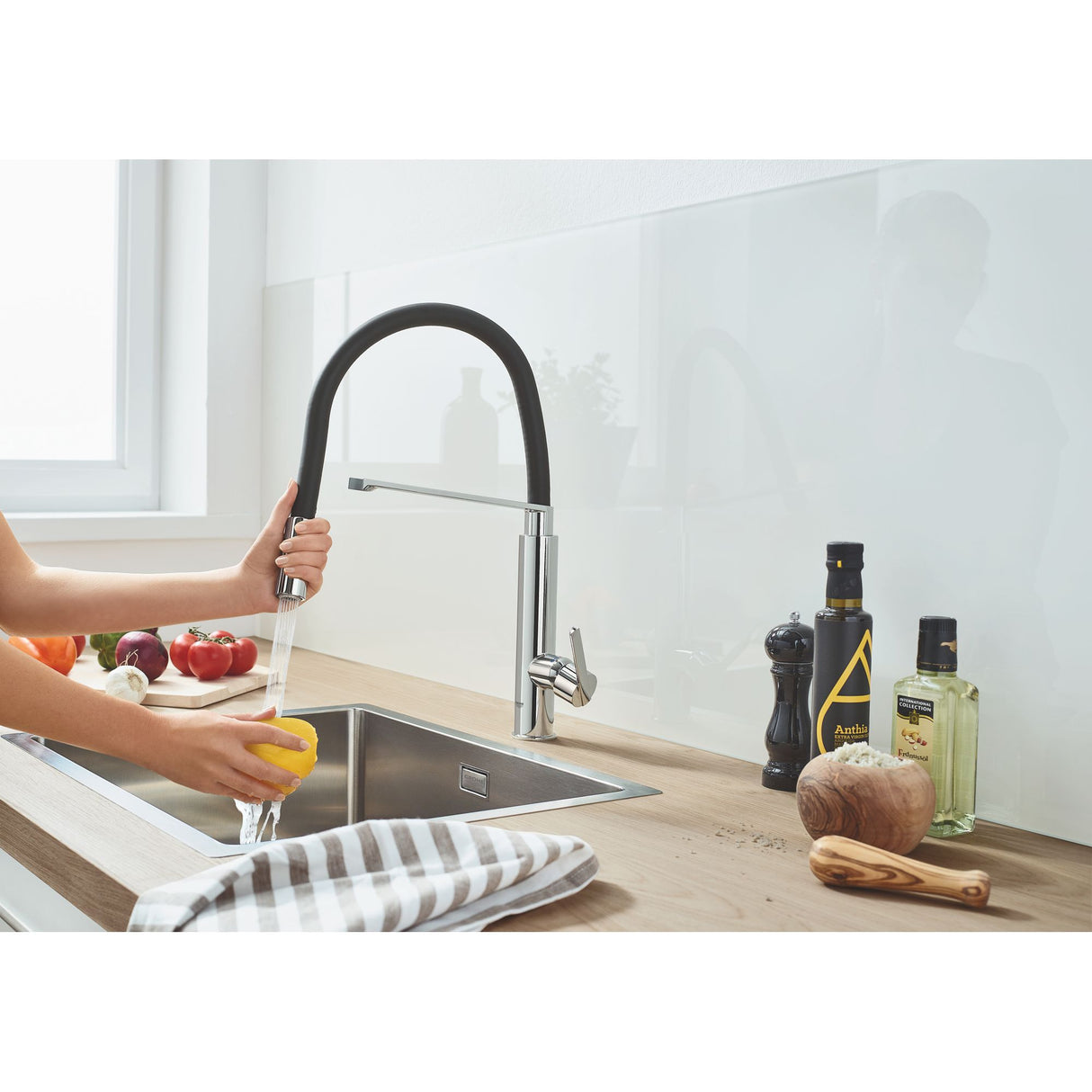 Mitigeur de cuisine Grohe, noir et chrome, sur évier moderne, mains rinçant un citron