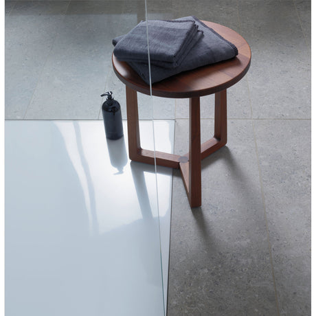 Receveur de douche blanc, marque inconnue, avec table d’appoint marron et serviettes grises.