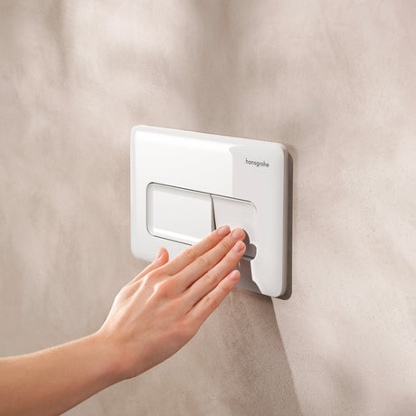 Plaque de déclenchement blanche Hansgrohe pour WC, main activant le mécanisme.