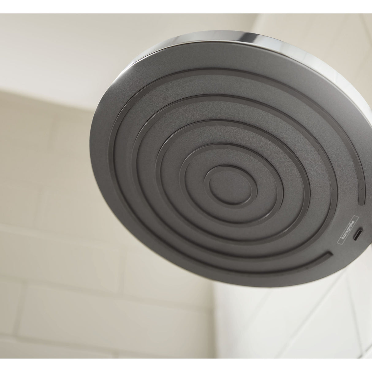 Pommeau de douche Impey, gris, de forme ronde, installé sur carrelage mural blanc.