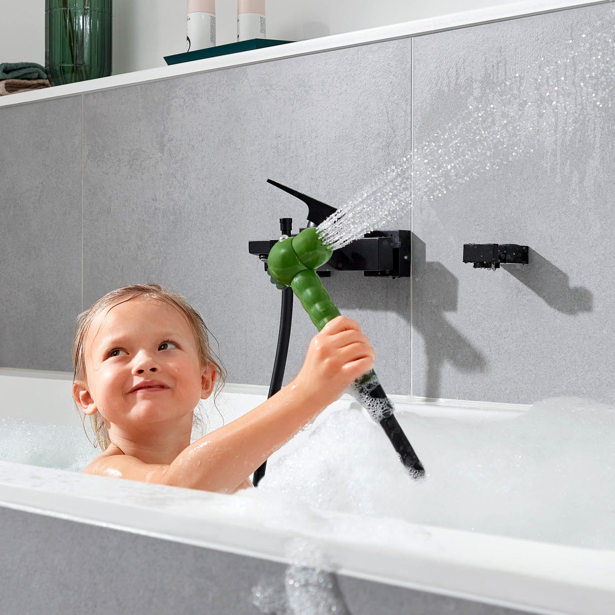 Douchette Grohe verte, accessoire de bain pour enfant, utilisée dans une baignoire.