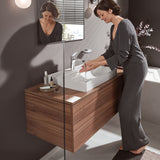 Femme utilisant un mitigeur Grohe, robinet de salle de bain chromé, sur meuble lavabo bois.