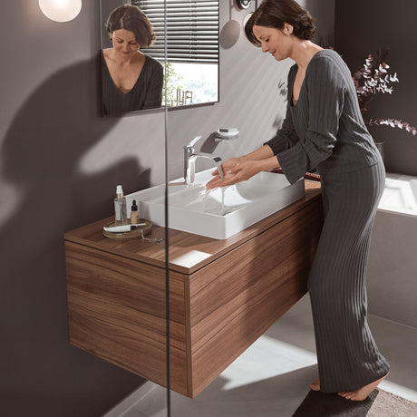 Femme utilisant un mitigeur Grohe, robinet de salle de bain chromé, sur meuble lavabo bois.