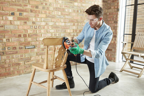 Ponceuse électrique Black+Decker orange, outil de bricolage pour bois, utilisée sur une chaise