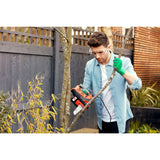 Homme utilisant une tronçonneuse Black+Decker orange et noire pour couper une branche d'arbre