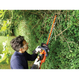 Taille-haie Black+Decker orange en utilisation pour tailler des haies vertes