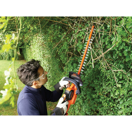 Taille-haie Black+Decker orange en utilisation pour tailler des haies vertes