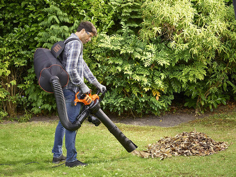 Homme utilisant un souffleur aspirateur Black+Decker orange et noir pour feuilles mortes dans un jardin