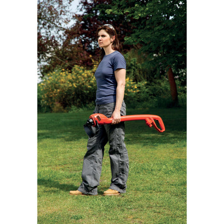 Coupe-bordures rouge Black & Decker tenu par une femme dans un jardin, outil de jardinage