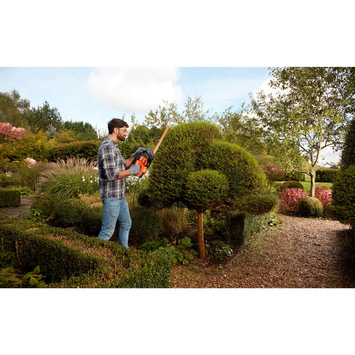 Taille-haie orange Black+Decker utilisé pour la taille de haies dans un jardin.