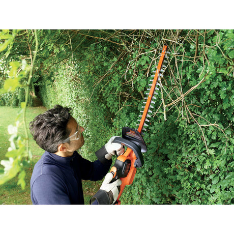 Taille-haie électrique Black+Decker orange utilisé pour tailler des haies vertes
