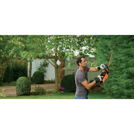 taille-haie Black+Decker orange utilisé pour tailler des haies vertes dans un jardin