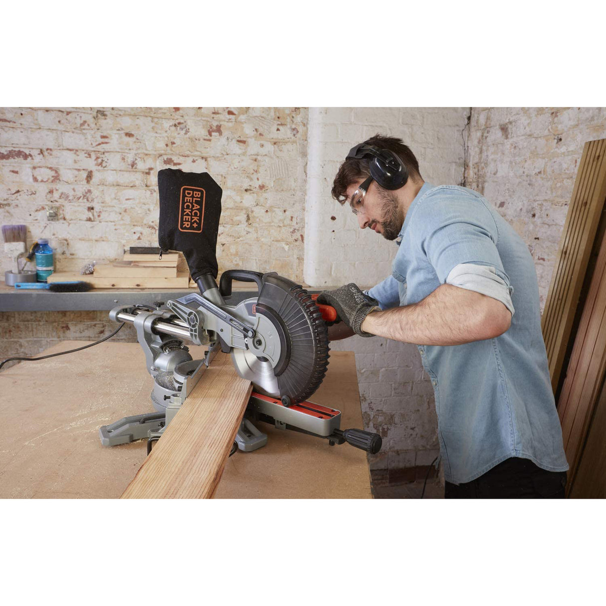 Scie à onglet grise Black+Decker en action sur une planche de bois, atelier bricolage.