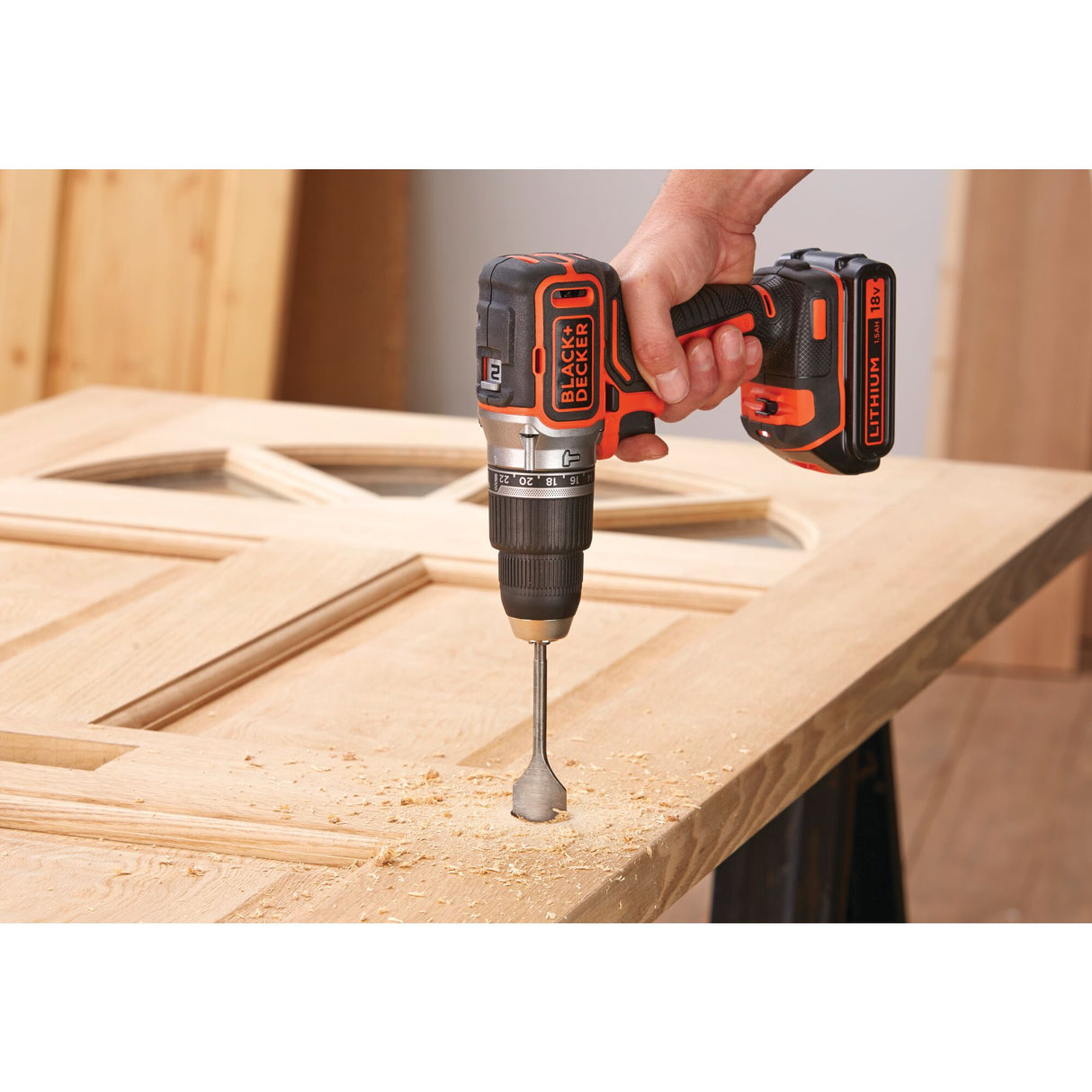 Perceuse BLACK+DECKER, perceuse-visseuse sans fil, couleur noire et orange, en action sur une porte en bois.