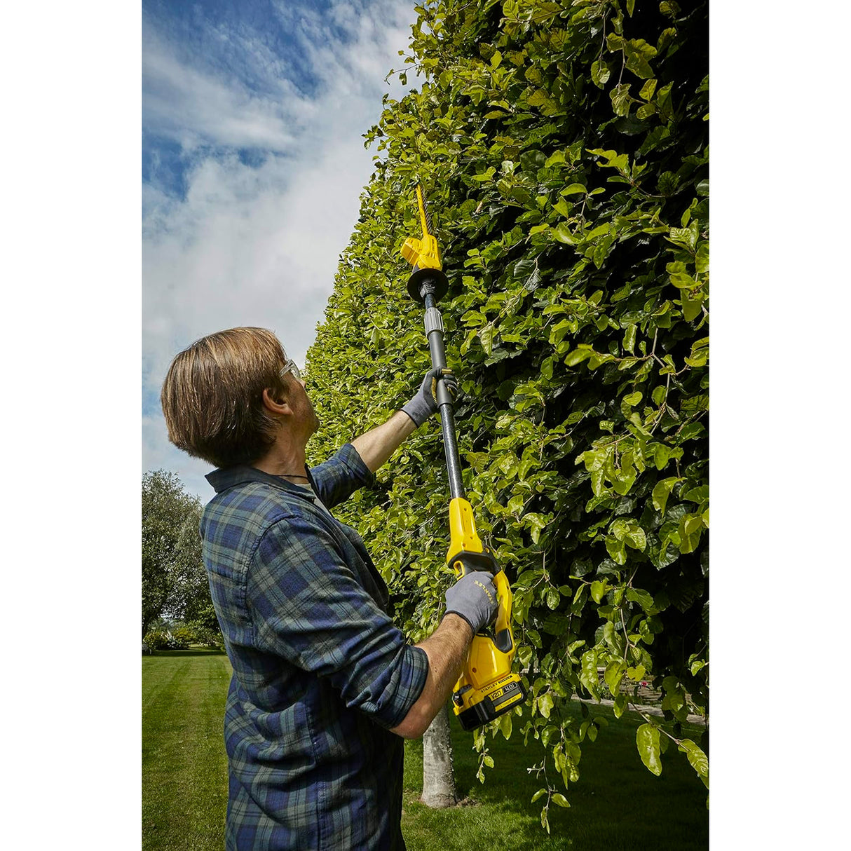 Taille-haie télescopique jaune de marque DeWalt utilisé pour tailler une haie