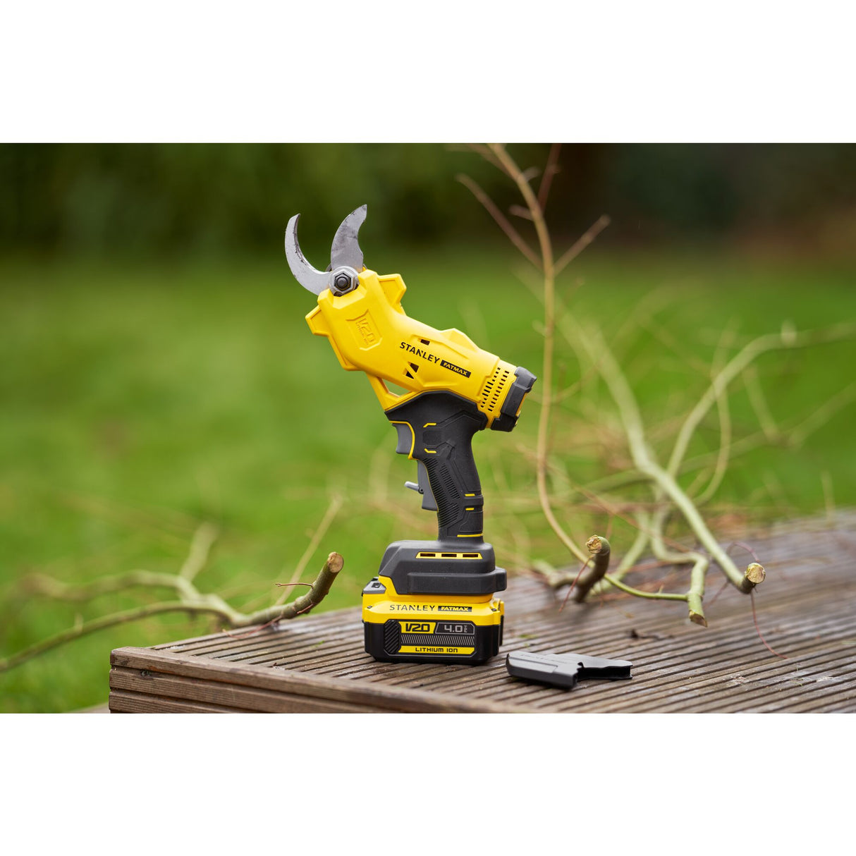 Sécateur électrique Stanley, couleur jaune et noir, posé sur une table en bois dans un jardin.