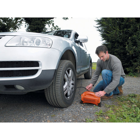 Homme utilisant un compresseur d'air orange Black+Decker pour gonfler un pneu de voiture