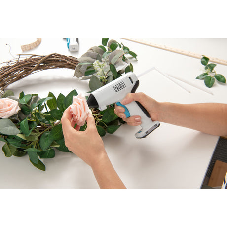 Pistolet à colle blanc Black+Decker utilisé pour coller une fleur sur une couronne de feuilles.