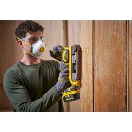 Ponceuse sans fil Stanley jaune utilisée pour poncer une porte en bois