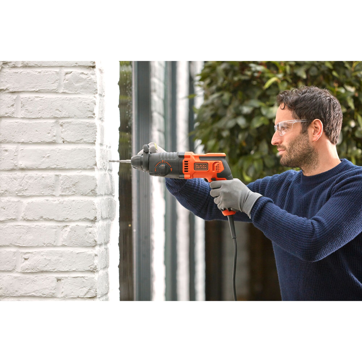 Perceuse filaire Black+Decker orange et noire en utilisation sur mur blanc