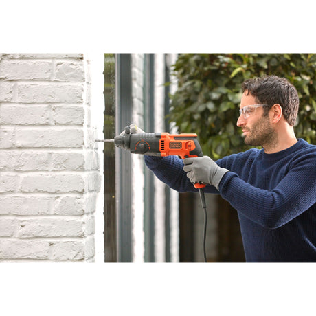 Perceuse filaire Black+Decker orange et noire en utilisation sur mur blanc