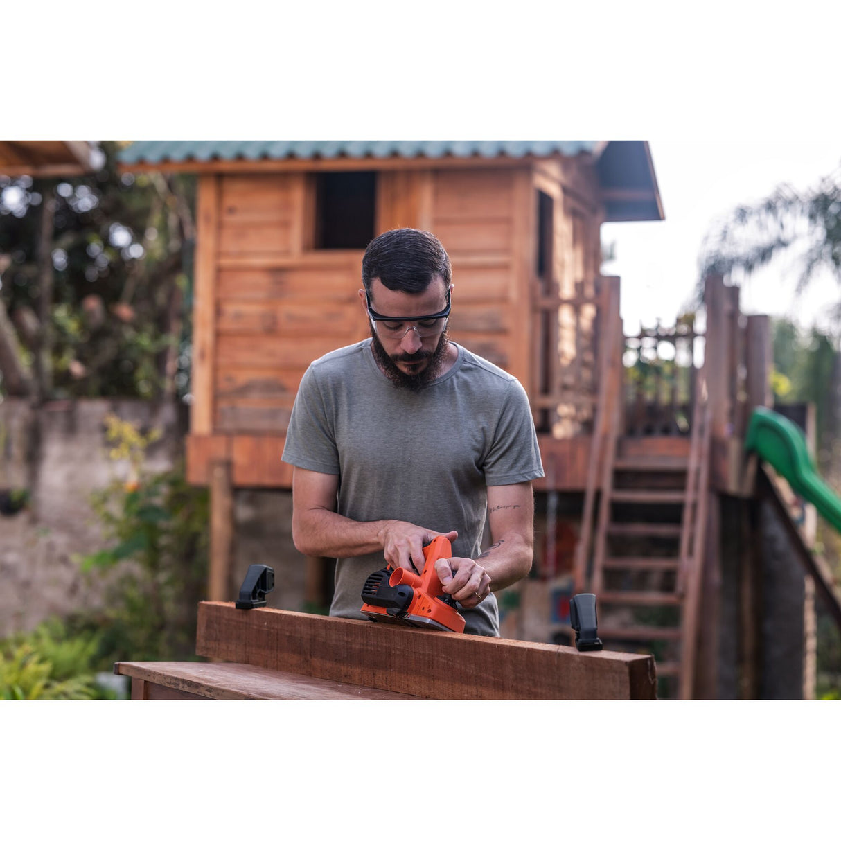 Homme utilisant un rabot électrique Black+Decker orange sur bois, outil électroportatif