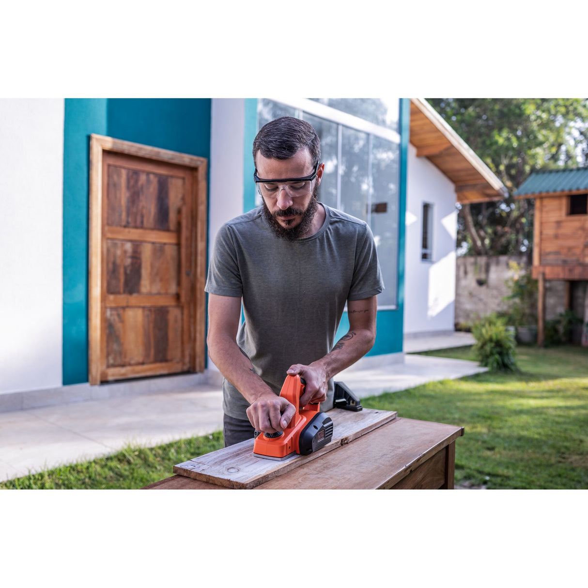 Homme utilisant un rabot électrique Stanley orange pour le bois dans un jardin