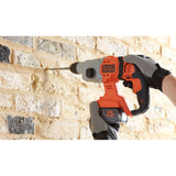 Perceuse-visseuse Black+Decker orange et noire sans fil en action sur mur de briques.