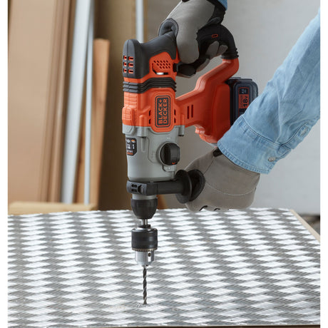 Perceuse BLACK+DECKER, type perforateur, couleur orange et noire, en utilisation sur métal.