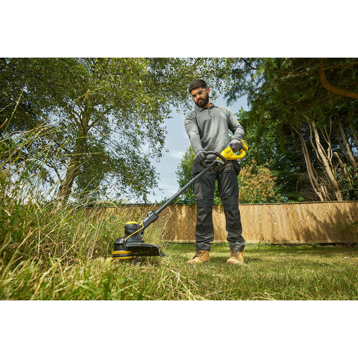 Débroussailleuse DEWALT jaune et noire utilisée par un homme dans un jardin, outil électrique.