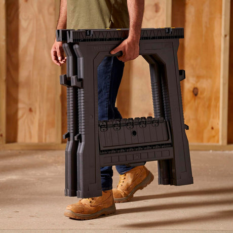 Tréteau pliant noir Stanley, outil de support portable, porté par un homme sur chantier