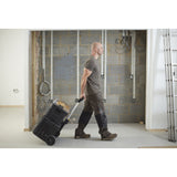 Homme tirant une boîte à outils noire Stanley sur roues, valise de chantier robuste, intérieur en construction.