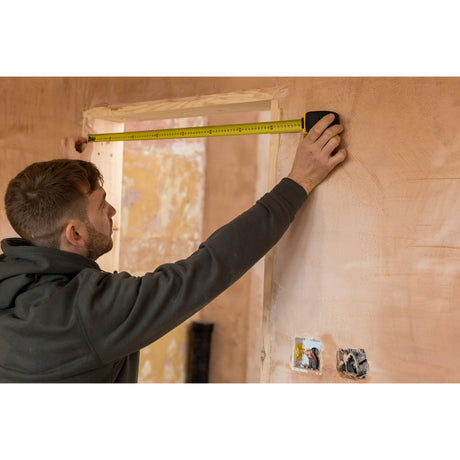Mètre ruban Stanley jaune, outil de mesure, utilisé par un homme sur un mur beige