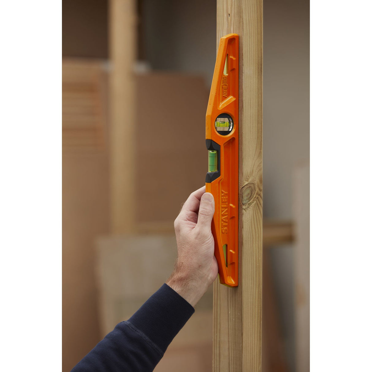 Niveau à bulle Stanley orange utilisé pour vérifier la verticalité d’un poteau en bois