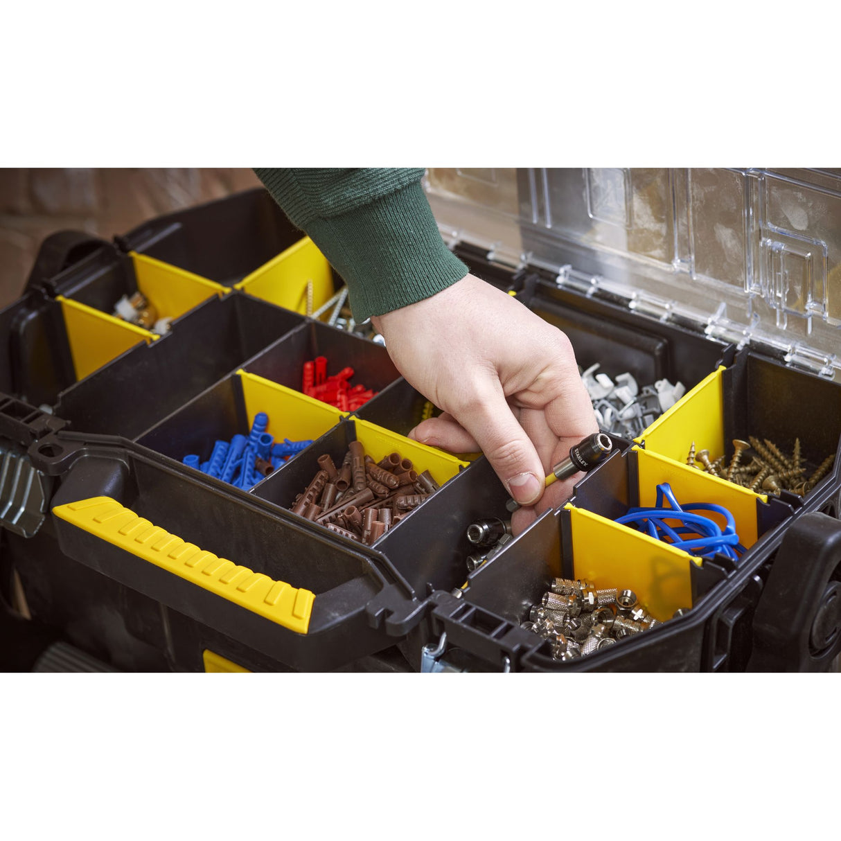 Boîte à outils Stanley noire et jaune, rangement compartimenté avec accessoires, main en action