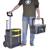 Coffre à outils Stanley, noir et jaune, portable et à roulettes, porté par un homme.