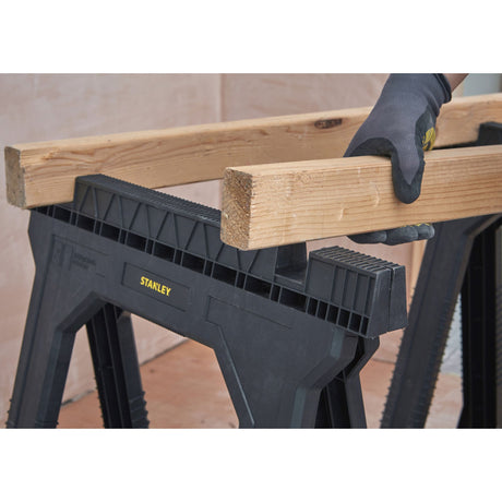 Tréteau noir Stanley en plastique, utilisé pour soutenir une poutre en bois.