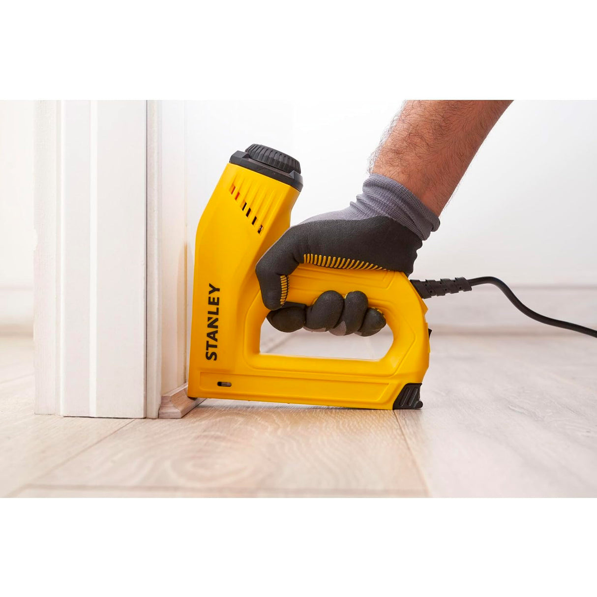 Agrafeuse électrique Stanley, outil jaune, utilisée sur un parquet, marque visible