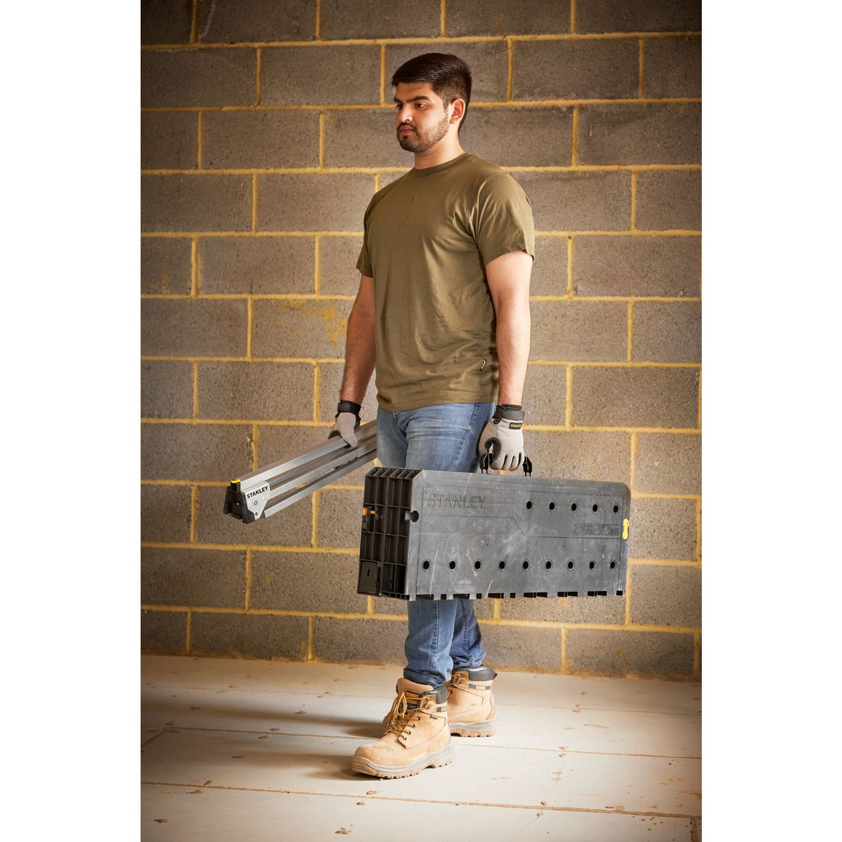 Homme portant un établi pliant noir Stanley, outillage portable, couleur noir