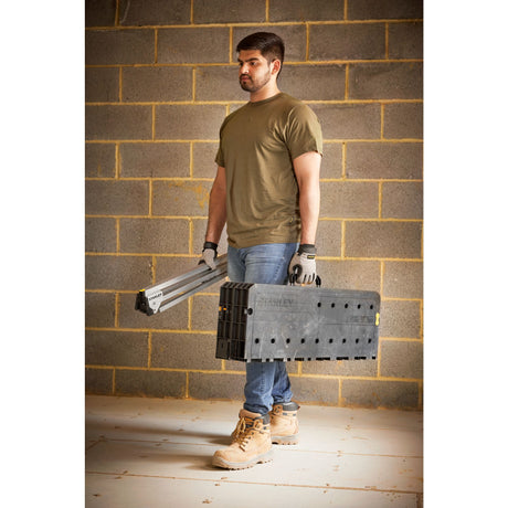 Homme portant un établi pliant noir Stanley, outillage portable, couleur noir